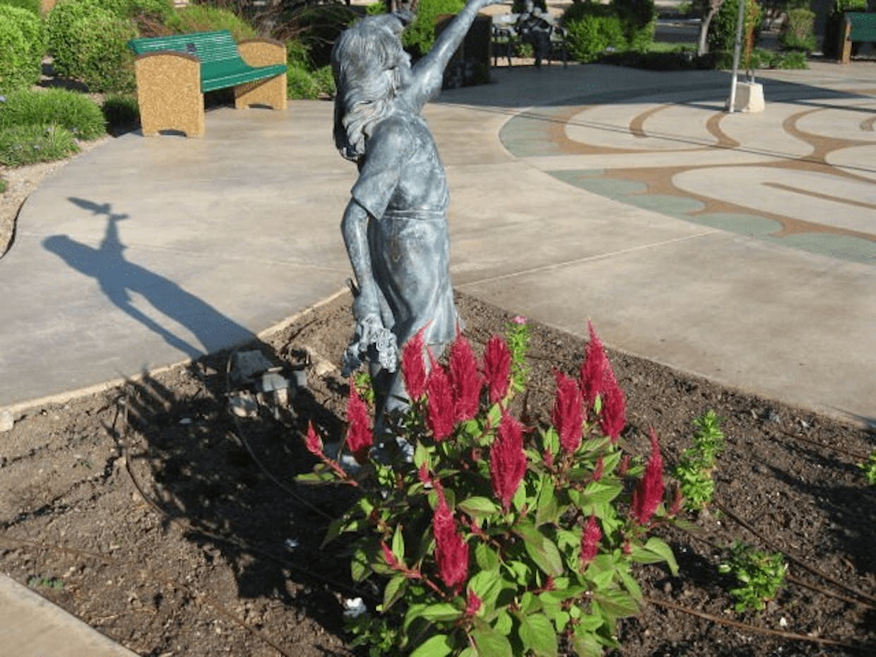 Patriotic red Celosia flowers highlight this small statue in Park Centre on the La Posada campus. (Mary Kidnocker photo)