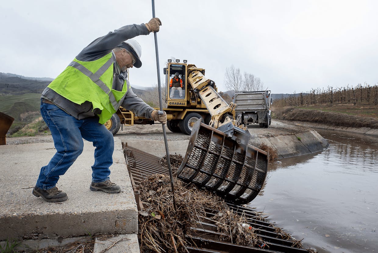 World photo/Don Seabrook Marty Howard with the Wenatchee Reclamation District pulls trash off of a brush rack as water flows into the irrigation ditch for the first time this year above Sunnyslope Monday, April 4, 2022. Nate Bratton operates a scoop in the background.